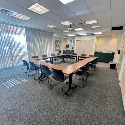 Meeting room with 8 tables on castors in a square shape with chairs surrounding. Large ceiling to floor windows and counter space. 