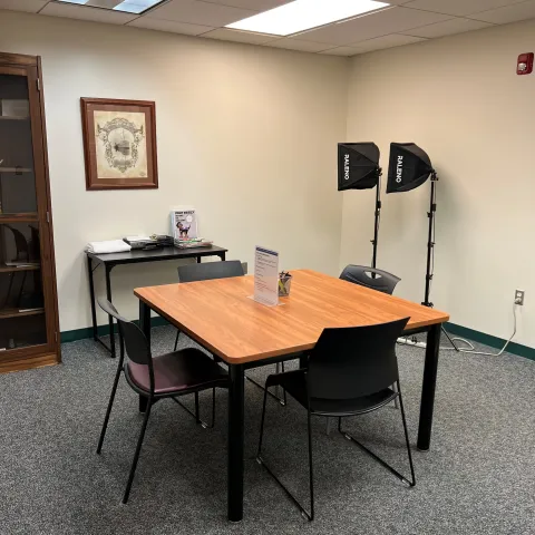 Passport Services room with a square table and four chairs, a small side table and two softbox lighting kits on tripods for passport photos.