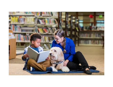 Child reading to adult and dog.