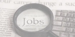 A magnifying glass highlights the word jobs on newsprint