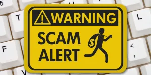 White keyboard overlaid with a yellow warning sign stating "Scam Alert"