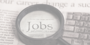A magnifying glass highlights the word jobs on newsprint