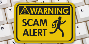 White keyboard overlaid with a yellow warning sign stating "Scam Alert"